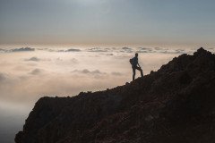 A lone hiker stands atop a rocky peak, silhouetted against a sea of clouds, embodying the spirit of adventure and the pursuit of breathtaking views.