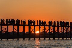 Silhouetted people gather on a bridge at sunset, likely to enjoy the view and capture photos of the scenic moment.