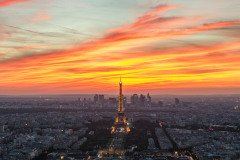 An aerial view of Paris, France, at sunset, with the Eiffel Tower illuminated in the foreground and the city skyline in the background.