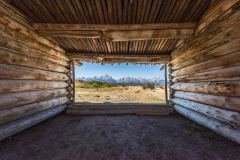 A view of the Grand Teton mountains from inside a log cabin.