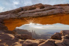 The sun shines through Mesa Arch in Canyonlands National Park, Utah, illuminating the landscape below.