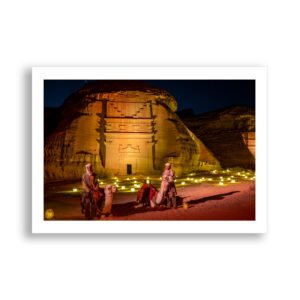 Two camel herders stand in front of a large tomb at Hegra, Saudi Arabia